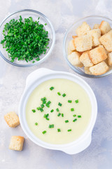 Potato leek soup in white ceramic bowl garnished with green onion served with croutons, vertical, top view