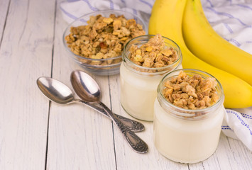 Yogurt with granola and banana on a white wooden background. The concept of dessert desserts. Top view.