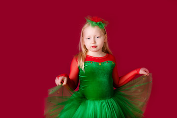 Beautiful little plump girl princess dancing in luxury green dress isolated on red background. Carnival party with costumes