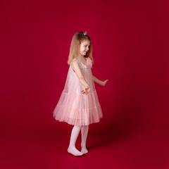 Beautiful little girl princess dancing in luxury pink and silver dress isolated on red background. Funny face, different emotions