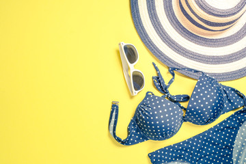 Summer travel vacation concept. Striped hat, swimsuit and sunglasses on yellow.