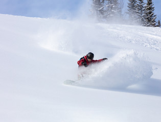 heliski snowboarding. freerider in a bright suit rides snowboarding with large splashes of snow on...