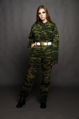 A girl soldier in camouflage clothing poses in a Studio