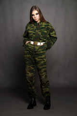 A girl soldier in camouflage clothing poses in a Studio