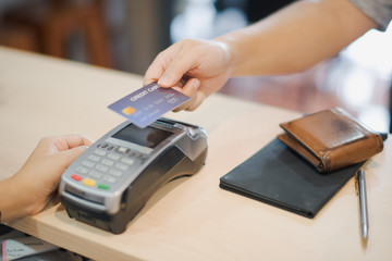 Hand of man customer using wireless or contactless payment of a credit card. Young Asian cashier or seller are smiling to accept payment by nfc technology at retail shop. Contactless payment concept.