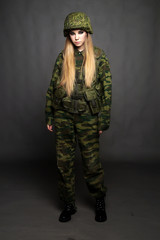 A girl soldier in camouflage clothing poses in a Studio