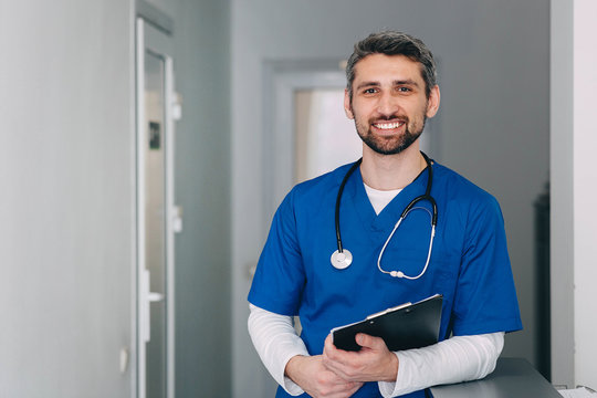 male nurse with stethoscope standing at clinic. He is smiling and looking at the camera.