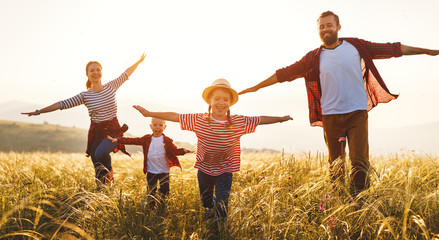 Happy family: mother, father, children son and daughter runing and jumping on sunset