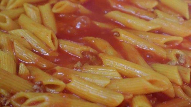 Close-up of cooking Italian pasta, macaroni slowly boiling in Bolognese tomato sauce.