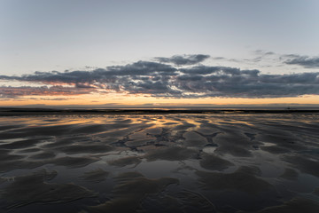 Panorama of a sunset reflected in pools on the sand with the Isle Of Man in the distance