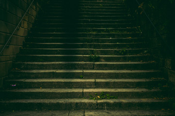 Breite Treppe in einem Park aus Naturstein mit Handlauf aus verrostetem Stahl im Dämmerlicht mit gruseliger und angsteinflößender Aura wie in einem Krimi - obrazy, fototapety, plakaty