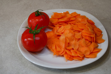 Vegan and vegetarian food. Plate of rawness with carrots cut into slices. Cooked tomato, peeled, skinless.