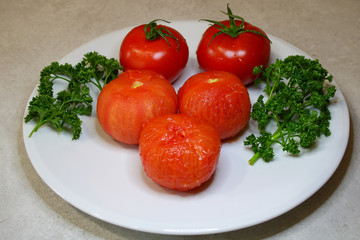 Vegan and vegetarian food. Plate of rawness. Tomatoes fresh red and peeled after cooking. Branches of green parsley.