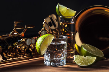 Saxophone and tequila with lime on a wooden table.