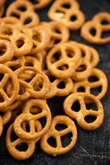 Close-up of pretzels with sea salt, vertical shot on a dark brown stone surface, selective focus
