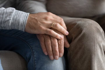 Young man put hand on wrinkled older senior fathers hand.