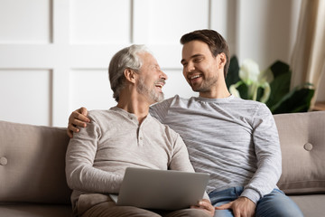 Happy elderly man holding computer enjoying fun time with son.