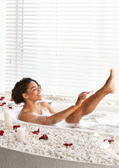 Obraz na płótnie Canvas Pretty black young woman shaving legs while taking bath
