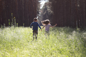 Boy and girl are running through the green forest, holding hands.