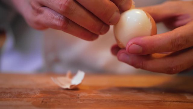 cook peels an egg on a wooden board.