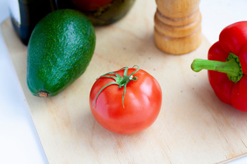 Tomato, in the background red sweet pepper, avocado, pepper shaker and a jar of pickled tomatoes