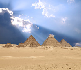Sun shines from clouds above the Giza pyramid complex.