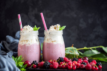 2 jars of milkshake or smoothie with cranberries, strawberries and blueberries standing on stone backdrop.