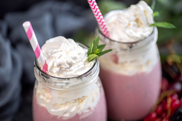 2 jars of milkshake or smoothie with cranberries, strawberries and blueberries standing on stone backdrop.