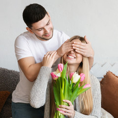 Man gifting his wife tulips flowers and covered her eyes