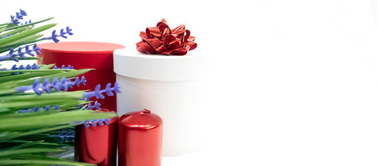 Festive background with flowers, white gift box with red bow, red gift box and red holiday candles on white background, copy space 