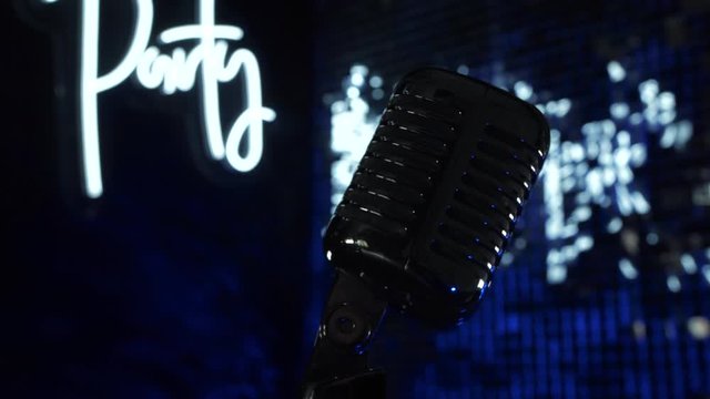 Disco vintage microphone on nightclub party stage on blurred glow and neon sign background. Music record concert studio in dark blue light, occupation object for modern club entertainment or lifestyle