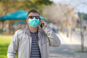 Man wearing medical mask. Male wearing medical mask in street in city and speaks on the phone. Male walking on the street wearing protective mask as protection against infectious diseases.