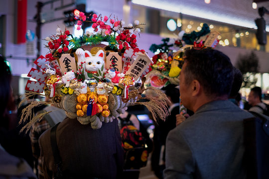 Japanese man in the crowd carrying colorful good fortune "Kumade" rake on his shoulder bought during Tori no Ichi festival at the precinct of Hanazono Shrine