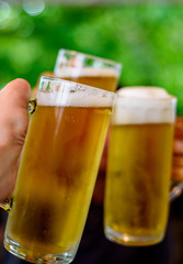 Close-up view of a three glass of beer in hand. Beer glasses clinking at outdoor bar or pub