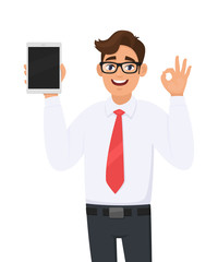 Young business man showing new tablet computer and making or gesturing okay, OK sign with fingers. Person holding a digital tab. Male character illustration. Modern technology in vector cartoon.