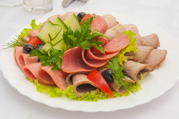 Fototapeta na wymiar slicing assorted sausages and meat with vegetables on a white plate
