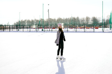 Young slim brunette skates on the ice and smiles