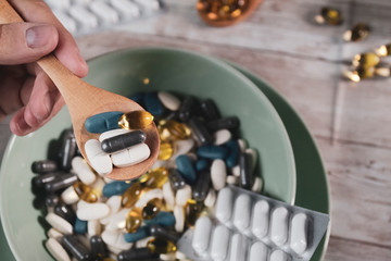 drug addiction, hand limp spoon full of pills, soup plate full of capsules capsules on wooden...