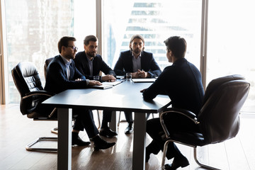 Applicant sitting in front three serious HR businessmen speaking.