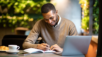 Black man writing in notebook sitting at cafe