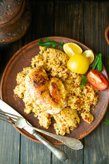 Grilled chicken thighs with couscous and herbs on a plate, vertical top view image