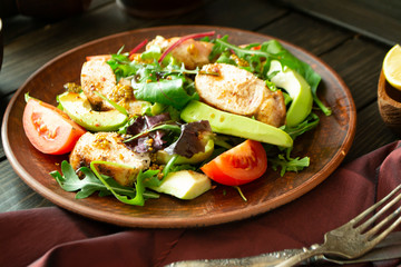 Chicken salad with avocado, arugula and tomato on a plate. Rustic style