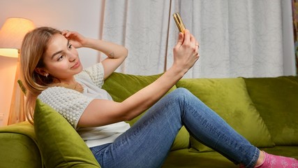 Attractive young playful woman taking a selfie on the couch. Hot female with beautiful smile and long hair having a video call.