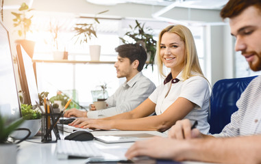 Cheerful blonde girl working in office, sitting next to colleagues