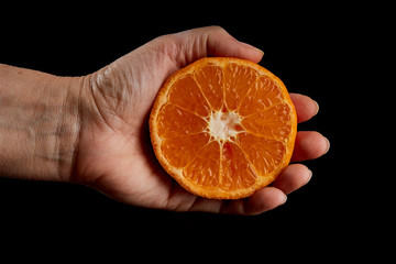 Sliced fresh, ripe mandarin fruit in hand, on black background