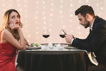 Unhappy woman sitting alone while her boyfriend stuck into his phone