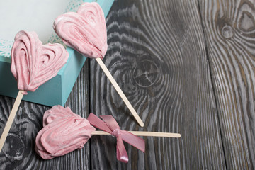 Delicate pink marshmallows in the shape of a heart on a stick. One with a ribbon tied to a bow. Near the turquoise color tray. Lies on brushed pine boards painted in black and white.