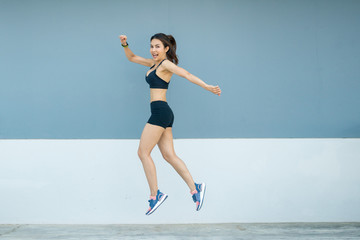 Beautiful young athletes are jumping in front of the indigo or gray and white background. She is...