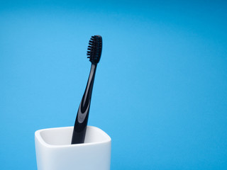One black toothbrush, for oral care, in a white toothbrush holder on a blue background