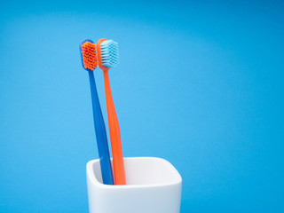 Two colored toothbrushes, blue and orange, for oral care, in a white toothbrush holder on a blue background